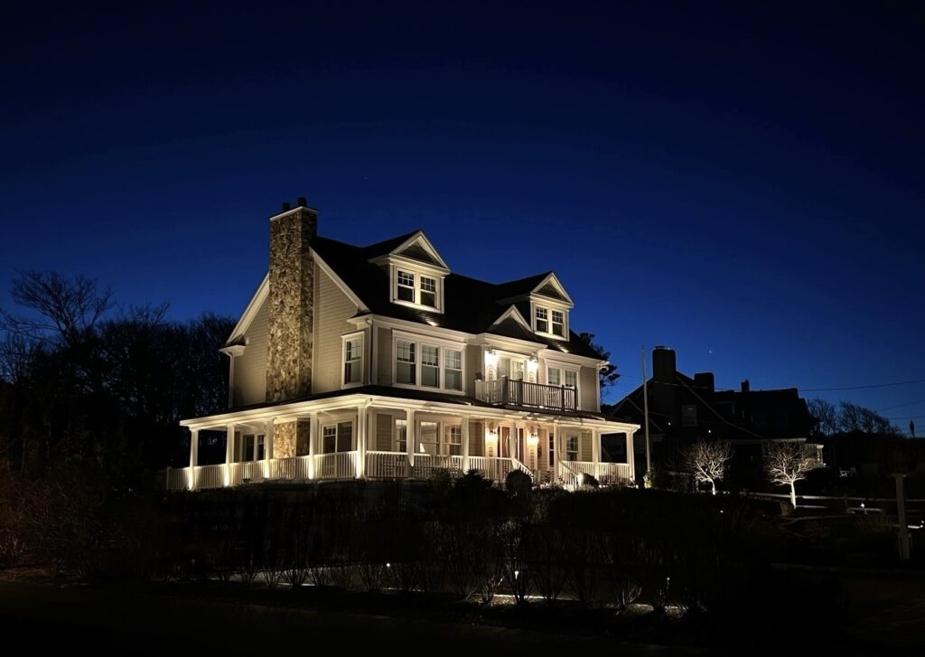 Outdoor lighting design highlighting a two-story home with porch and chimney at night.