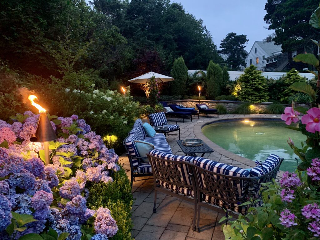  Backyard outdoor lighting design with pool, garden, and patio seating at dusk.