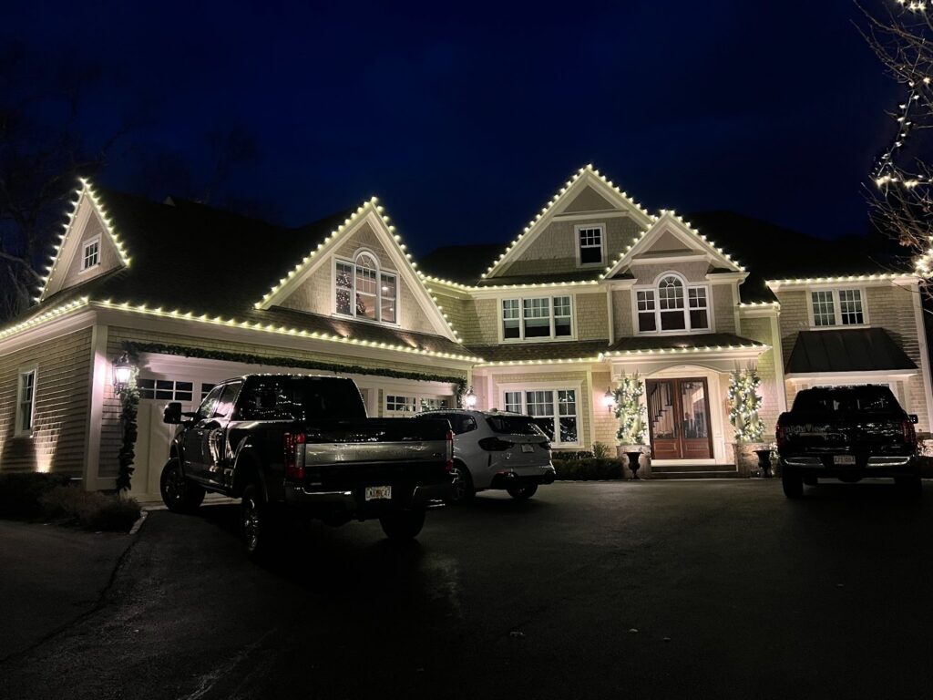 Professional holiday light installation on a Massachusetts home with custom warm white roofline lighting.